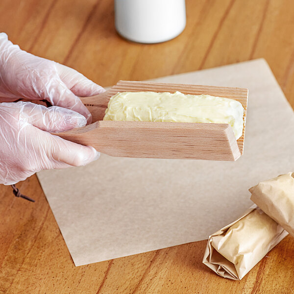 A person wearing gloves uses a Fox Run wood butter paddle to spread butter on a piece of bread.