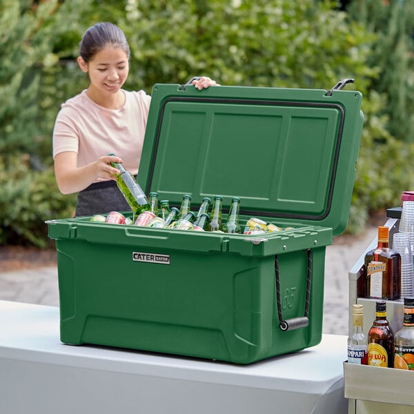A woman opening a CaterGator Hunter Green cooler to put bottles of beer inside.