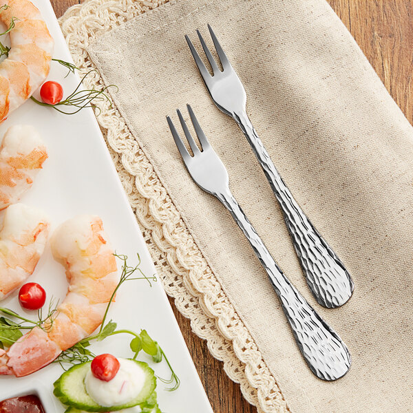A plate of shrimp and vegetables with an Acopa Inspira cocktail fork on a napkin.