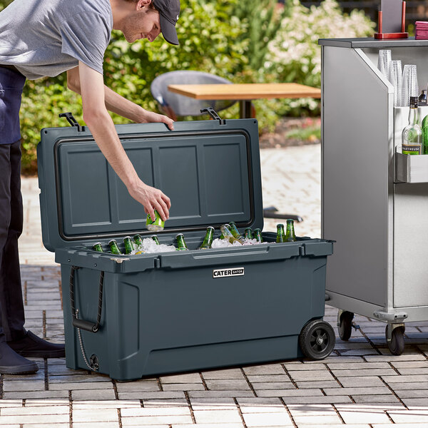 A man opening a CaterGator outdoor cooler to put bottles inside.