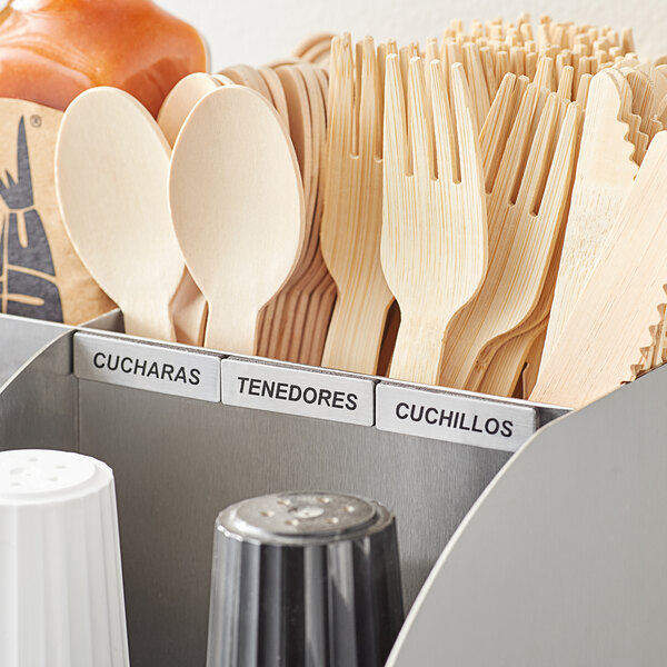 A white container with wooden utensils labeled in Spanish with a white magnetic label.