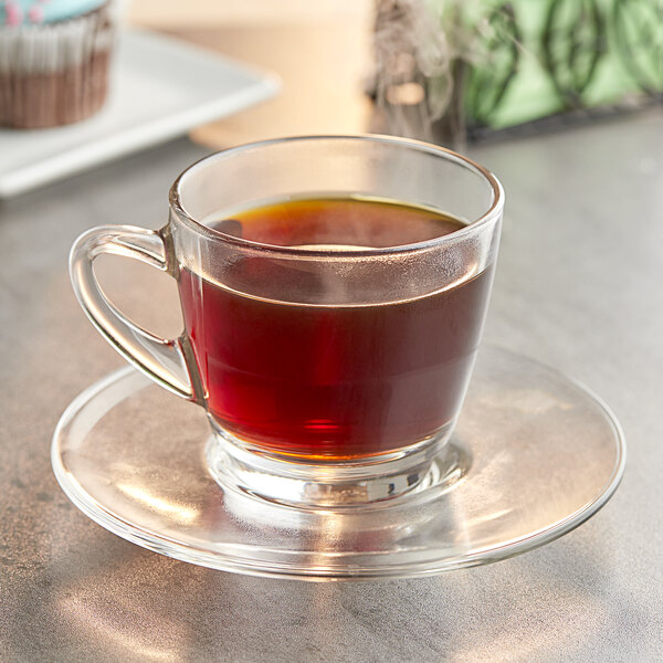 A glass cup of Crown Beverages Organic Donut Shop Coffee on a saucer on a table.