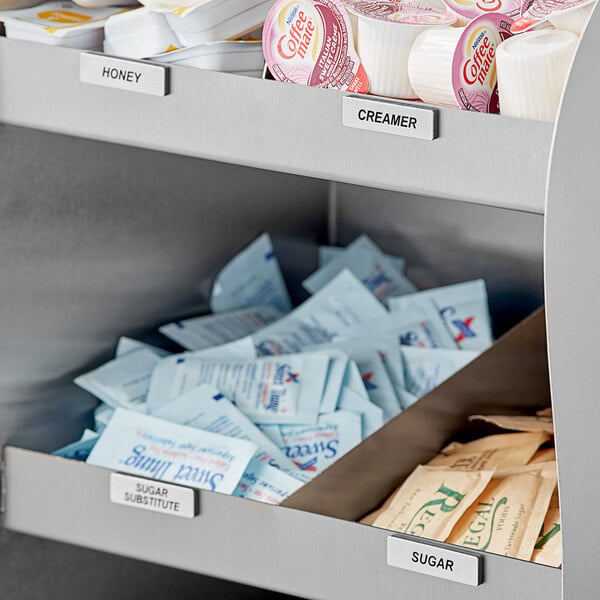 A metal shelf with ServSense stainless steel coffee labels on a counter with condiments and sugar packets.