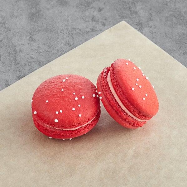 Two red Macaron Centrale macarons with white sprinkles.