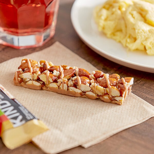 A KIND Caramel Almond & Sea Salt bar on a napkin next to a plate of food.