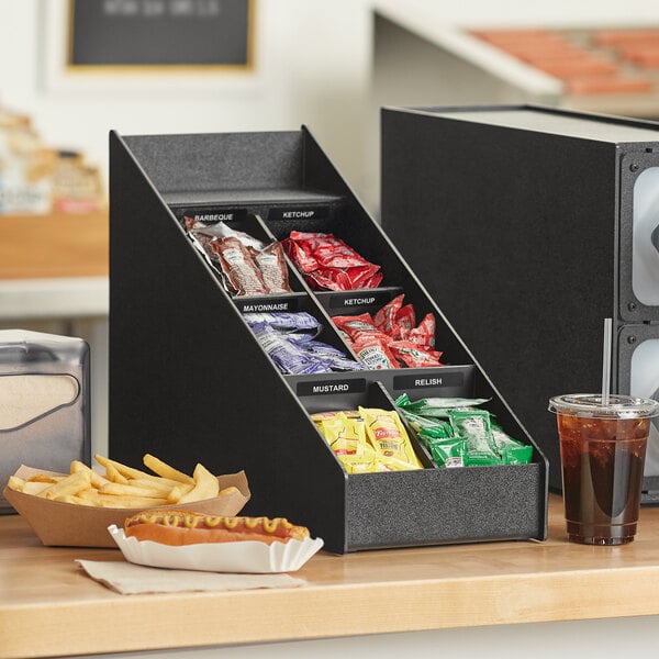 A black ServSense countertop condiment organizer with 6 sections holding condiments.