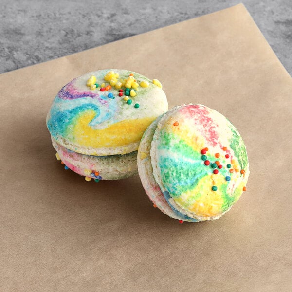 Two multicolored Macaron Centrale unicorn macarons with sprinkles on top.