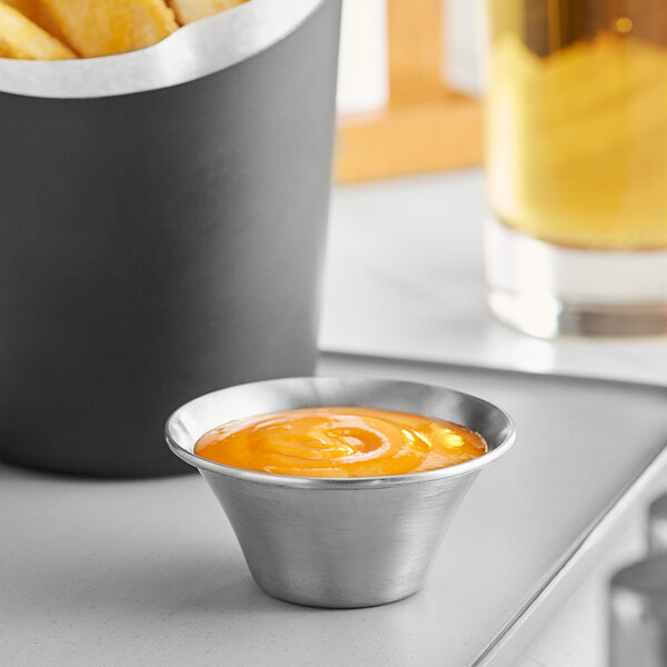 An American Metalcraft stainless steel sauce cup with fries and yellow liquid.