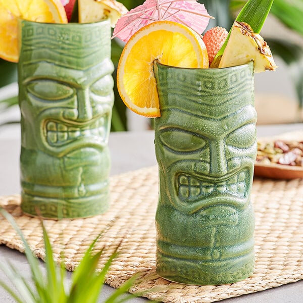 Two green Libbey Tiki Tumblers with fruit on a table.