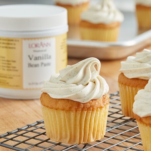 A vanilla cupcake with white frosting on a cooling rack.