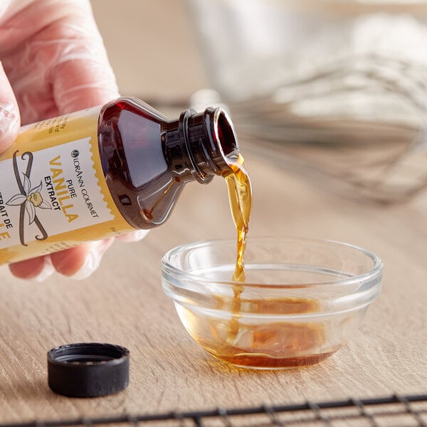 A hand pouring LorAnn Oils Pure Vanilla Extract from a bottle into a glass bowl.