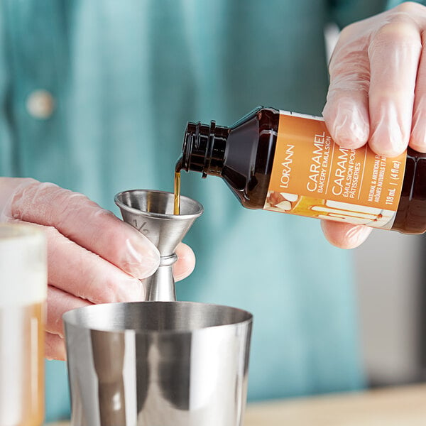 A hand pouring LorAnn Oils Caramel Bakery Emulsion into a metal measuring cup.