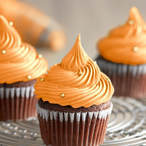 A group of cupcakes with orange frosting on a metal rack.
