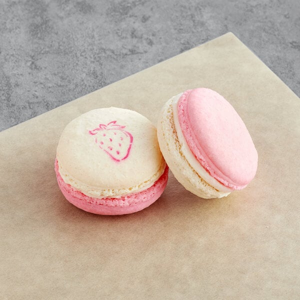 A close up of a strawberry sundae macaron with pink and white icing and a strawberry design on the top.
