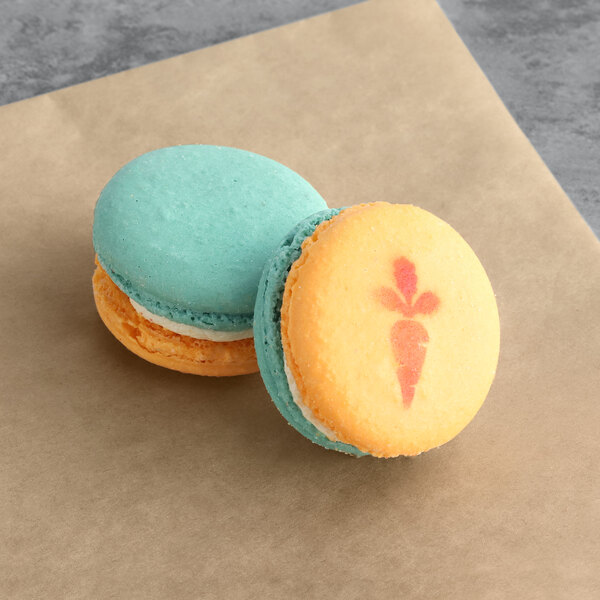 Two Macaron Centrale carrot buttercream macarons with carrot designs on top displayed on a brown surface.