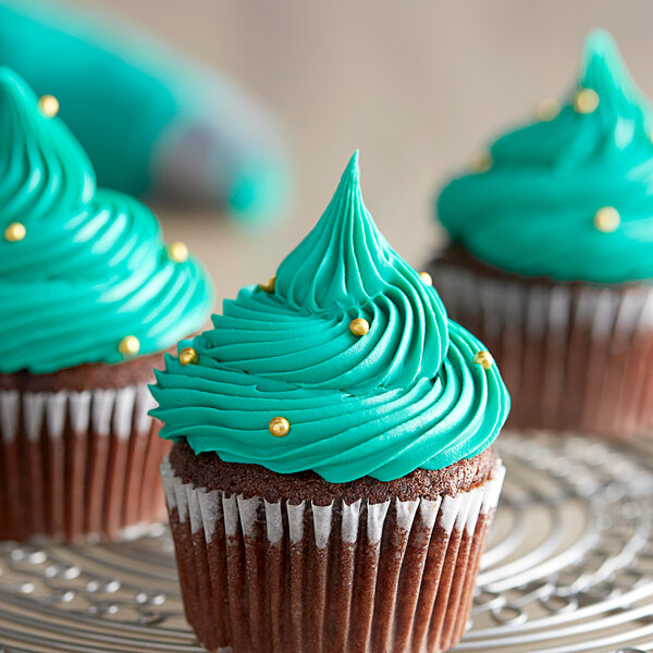 A cupcake with teal frosting and gold sprinkles on a silver plate.