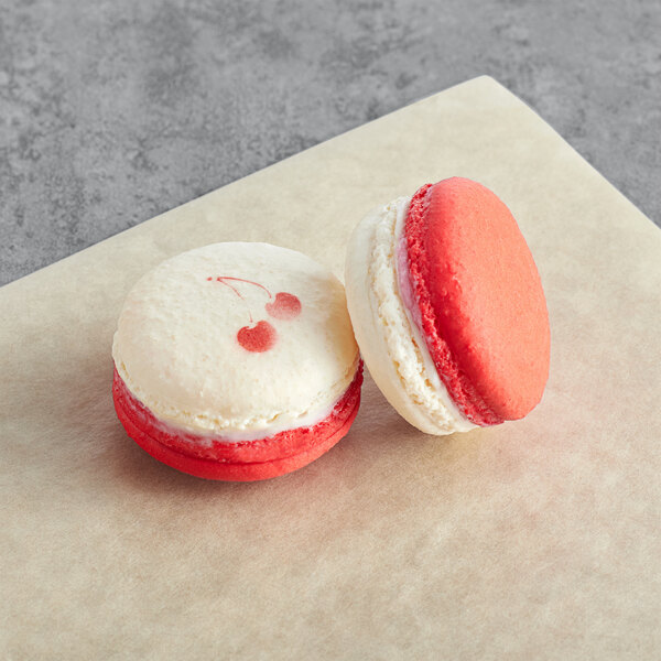 Two Cherry Sundae Macarons with pink and white icing on a piece of paper.
