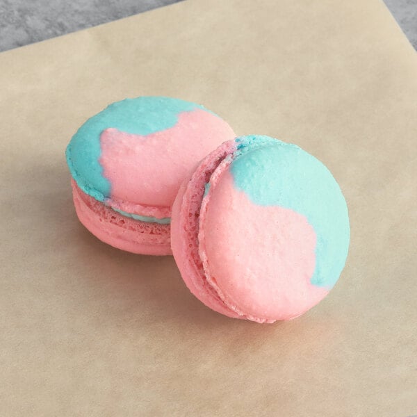 Two blue and pink Macaron Centrale macarons on a brown surface.