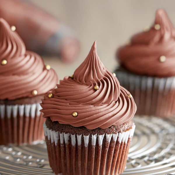 A chocolate cupcake with brown frosting on a wire rack.