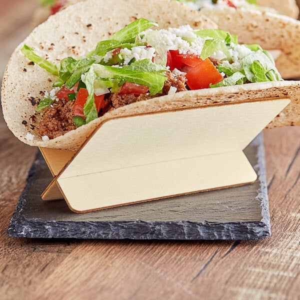 A Tablecraft Taco Taxi disposable poplar wood taco holder on a table with tacos.