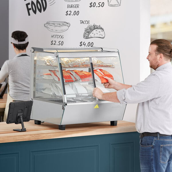 A man using a ServIt countertop heated display case to put food in a glass case.
