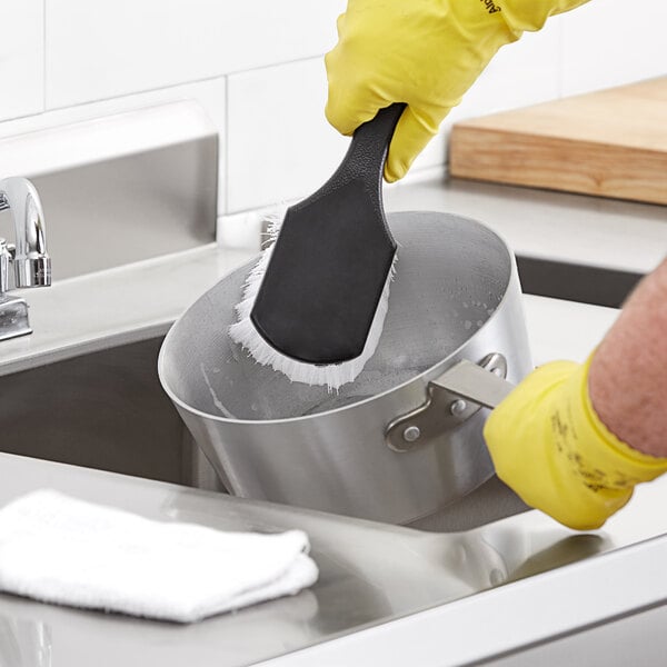 A person cleaning a pot with a Choice black polypropylene utility brush.