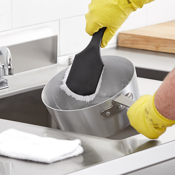 A person cleaning a pot with a black Choice nylon utility brush.