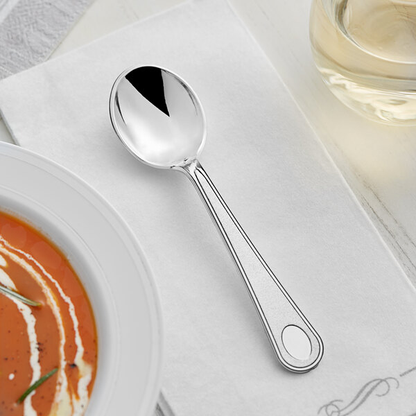 A Visions heavy weight satin plastic soup spoon on a white napkin next to a bowl of soup.