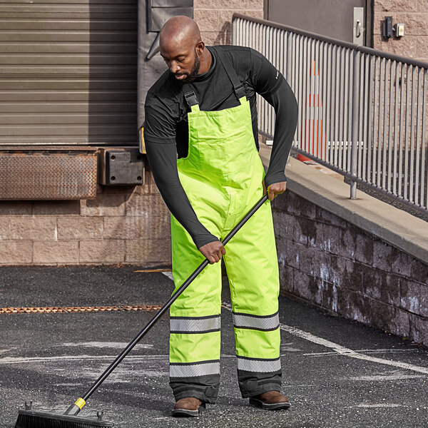 A person in yellow Cordova quilted bib pants sweeping a parking lot.