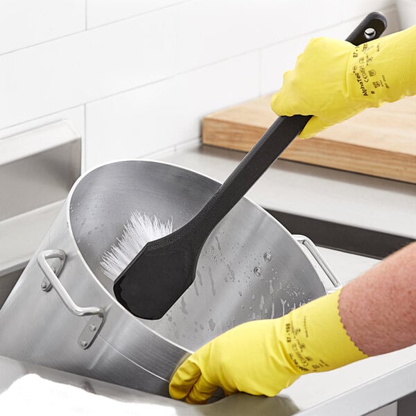 A person cleaning a pot with a Choice black nylon utility scrub brush.