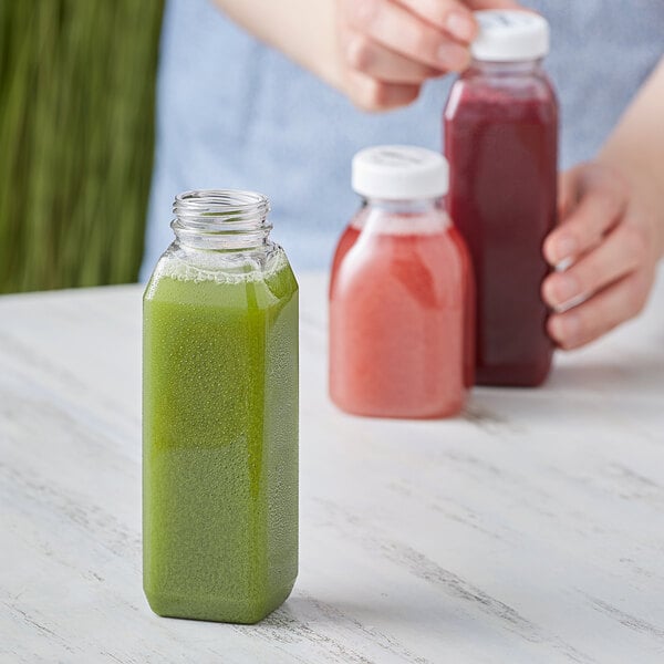 A woman pours green juice into a customizable square PET clear bottle.