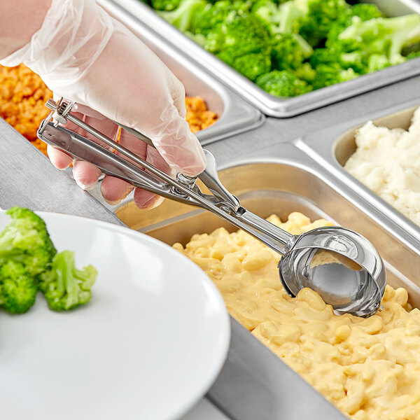 A person in gloves using a Choice stainless steel squeeze handle disher to serve macaroni and cheese in a school cafeteria.