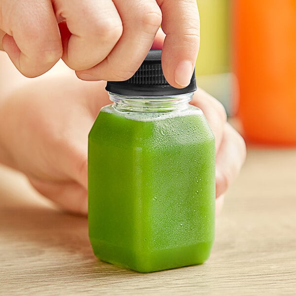 A hand holding a 4 oz. square PET clear energy juice bottle filled with green liquid.