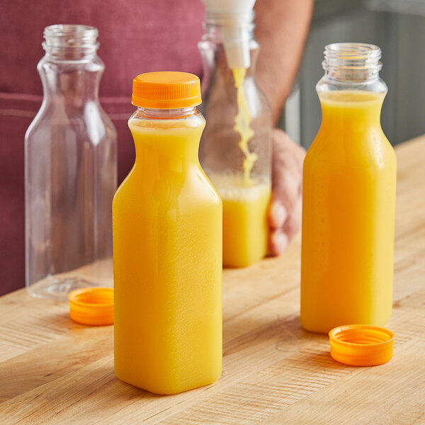 A man pouring orange juice into 12 oz. square juice bottles with orange caps on a table.