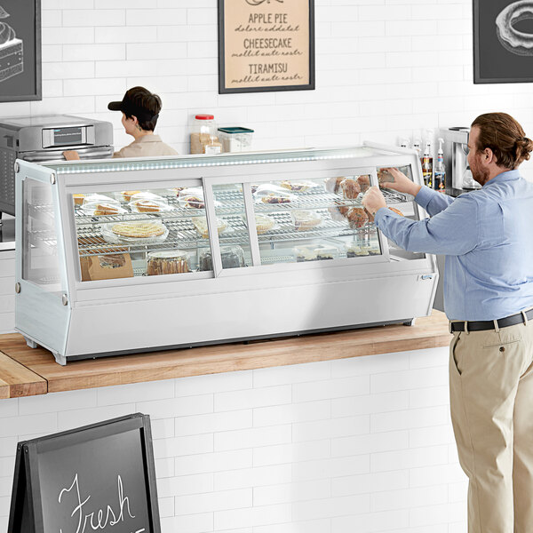 A man standing at a countertop with food in a white Avantco self-serve bakery display case.