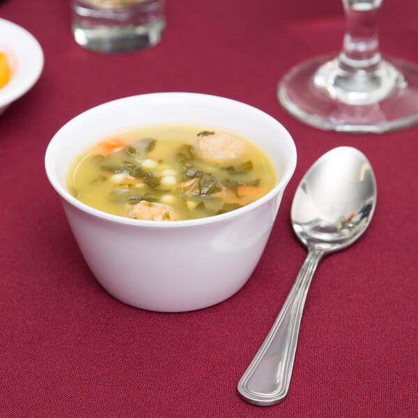 A white Carlisle Dallas Ware bouillon cup filled with soup with meatballs and vegetables with a spoon next to it.