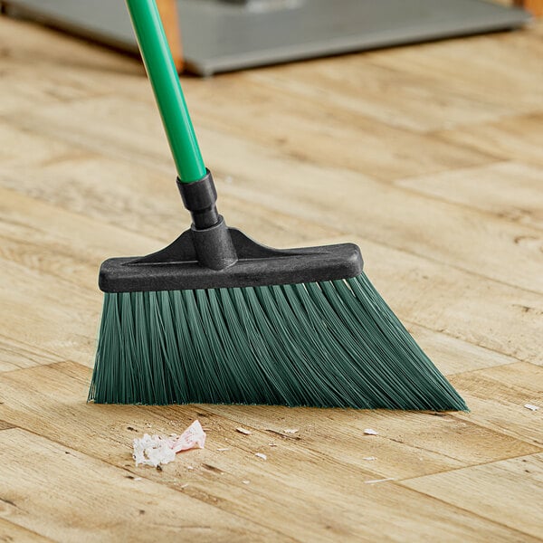 A Lavex green broom head on a wooden floor.