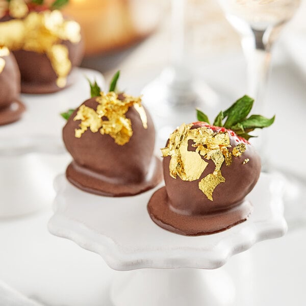 Chocolate covered strawberries with 24K edible gold leaf on a white plate.