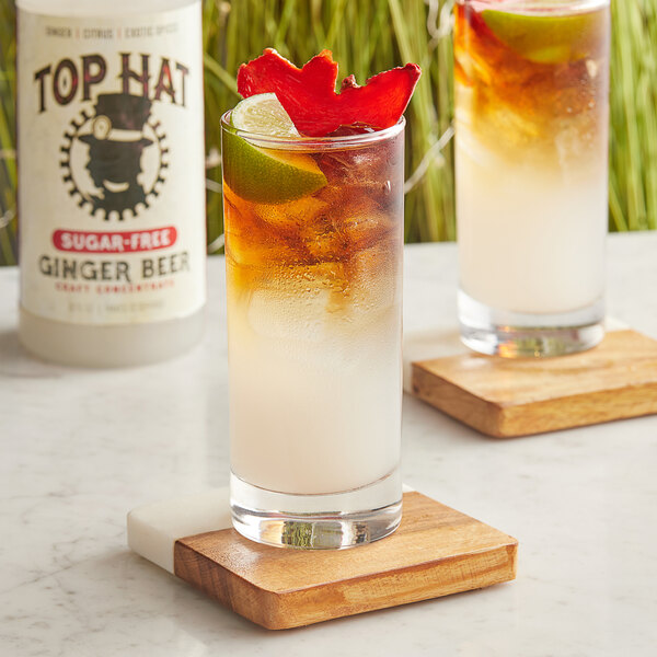 A glass of brown liquid on ice with a lime next to a bottle of Top Hat Provisions Sugar-Free Spicy Ginger Beer.