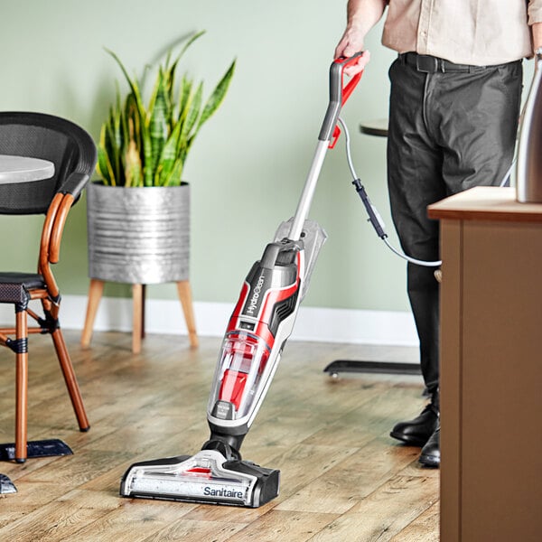 A man using a Sanitaire HydroClean hard floor washer/vacuum on a floor.