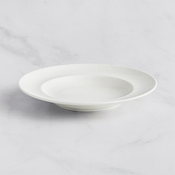 A RAK Porcelain ivory deep plate with an embossed rim on a white surface with a fork.