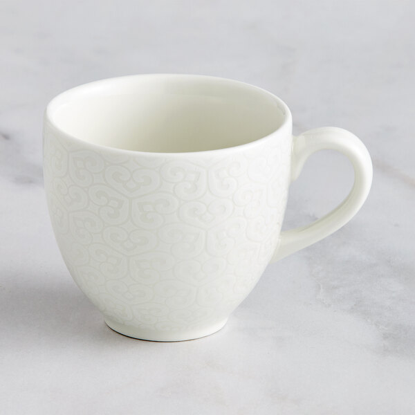 A close up of a RAK Porcelain ivory porcelain coffee cup with an embossed pattern and a handle.