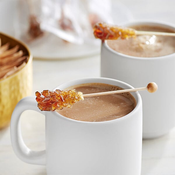 A white mug of coffee with a Roses Dryden and Palmer amber wrapped rock candy on the rim.