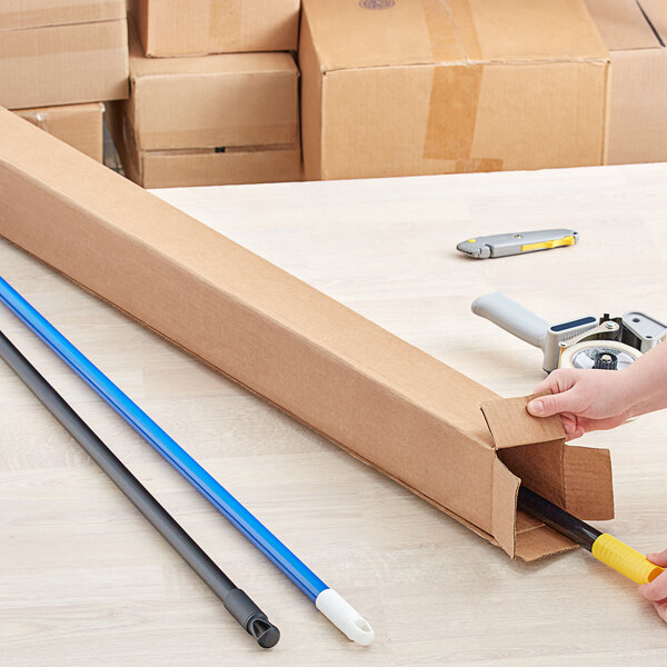 A hand using a box cutter to open a Lavex Kraft shipping box.