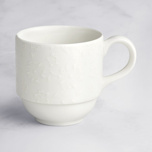 A close up of a white RAK Porcelain coffee cup with an embossed floral design on the handle.