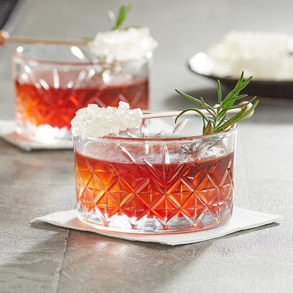 A crystal clear glass with a red liquid and a Roses Dryden and Palmer White Rock Candy swizzle stick garnish.