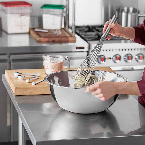 A woman mixing pasta in a Choice stainless steel mixing bowl.