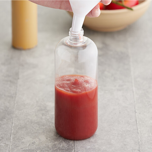 A hand pouring red sauce from a bottle into a glass.