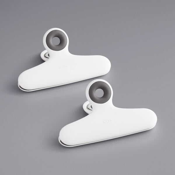 Two white OXO Good Grips bag clips on a gray surface.