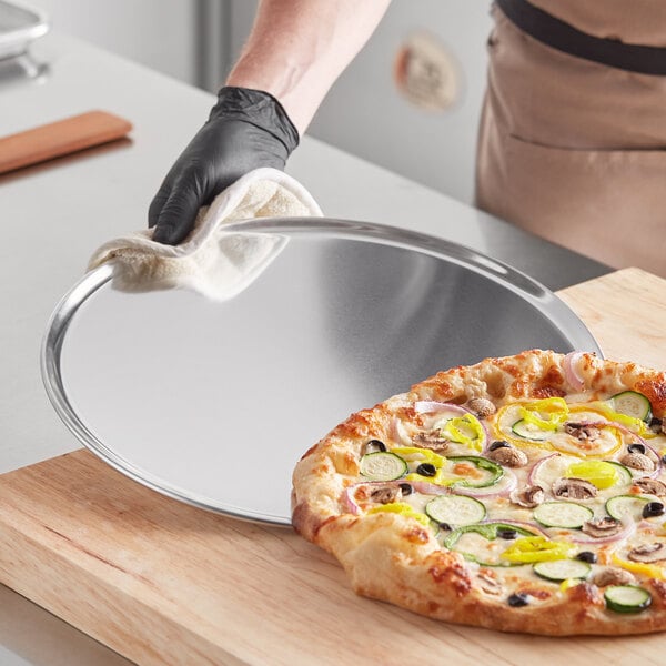 A person holding a pizza on a Choice aluminum coupe pizza pan.